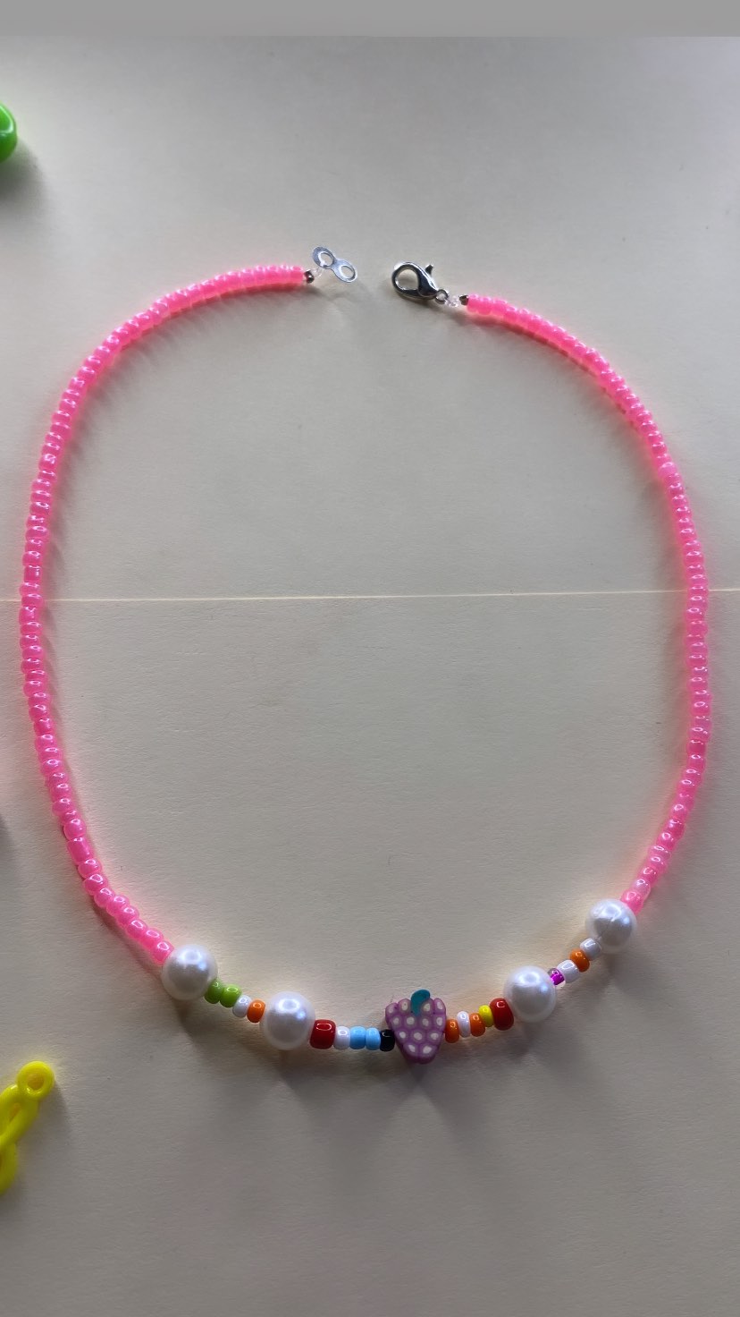 Colorful beaded necklace with a central purple grape-shaped bead and various other beads in pink, white, red, and yellow.